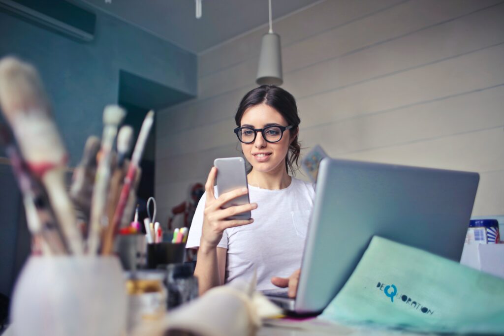Bilden visar en person på ett modernt kontor som sitter vid en dator och med en telefon i handen. Kontorspapper och kontorsprodukter till kontoret hittar du enkelt online.